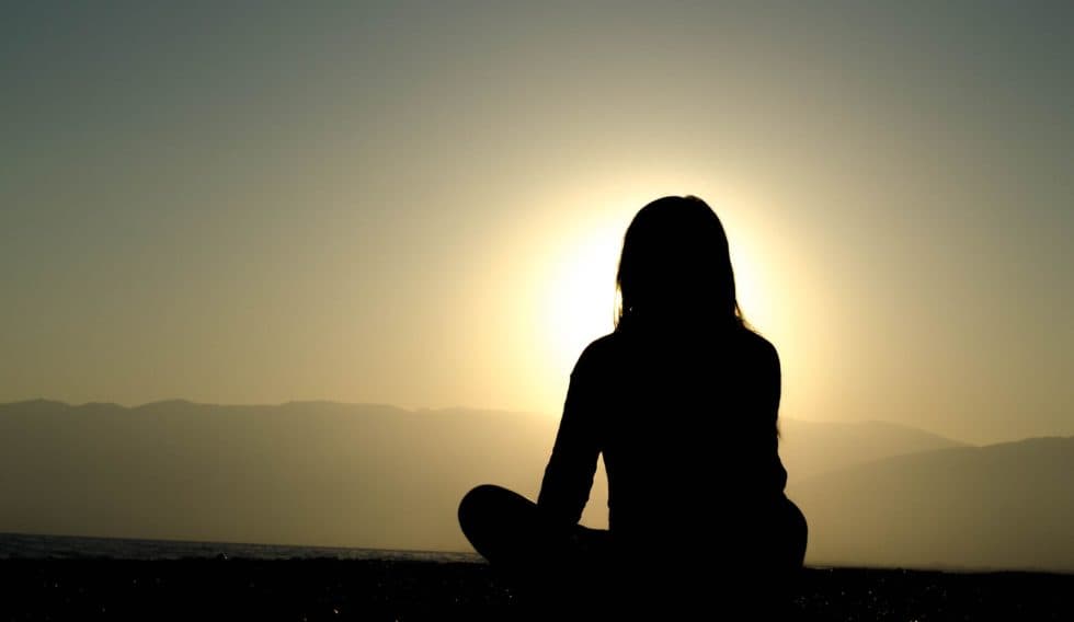 A person sitting in silhouette against a bright sunrise